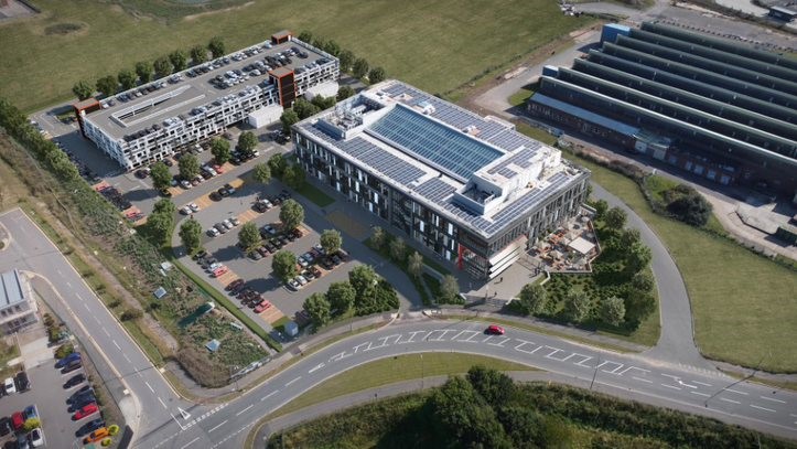 Aerial view of a modern, large office building (Cadent's headoffice in Ansty) with green landscaping, parking and solar panels, surrounded by open fields and industrial structures.